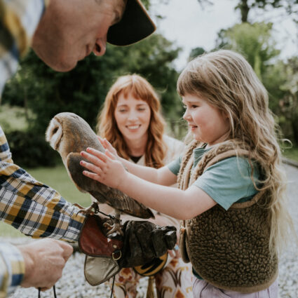 Child joyfully touches an owl with green gardens in the background, highlighting family-friendly activities at the hotel.