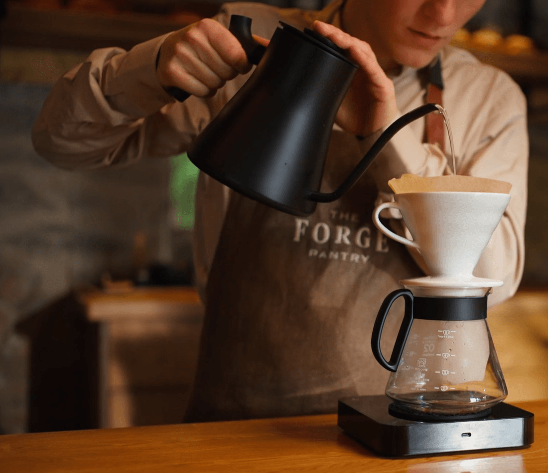 A barista at Dromoland Castle's café skillfully pours hot water into a ceramic dripper, brewing fresh coffee in an elegant, rural setting.