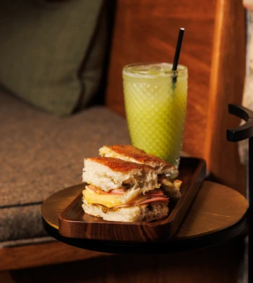 A gourmet sandwich with layers of cheese and ham on a wooden tray next to a frothy green beverage, set against a rustic backdrop. Dromoland, Newmarket on Fergus, Co. Clare, Ireland.