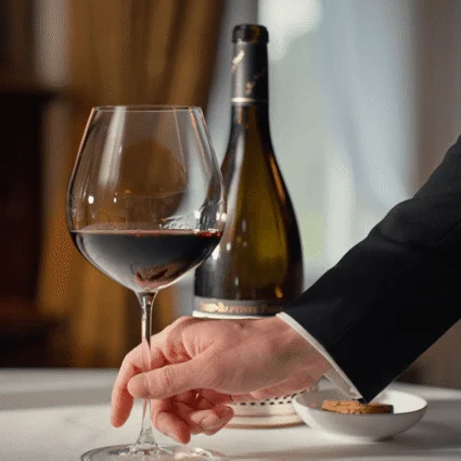 A guest elegantly pours wine from a bottle at Dromoland Castle, Ireland, set on a finely dressed table with ambient lighting, creating a refined atmosphere.