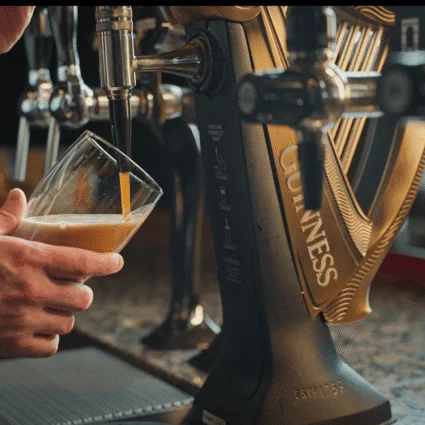 A bartender at Dromoland Castle skillfully pours a pint of Guinness, capturing the rich, creamy texture, set against an elegant bar with polished wood and brass detailing.